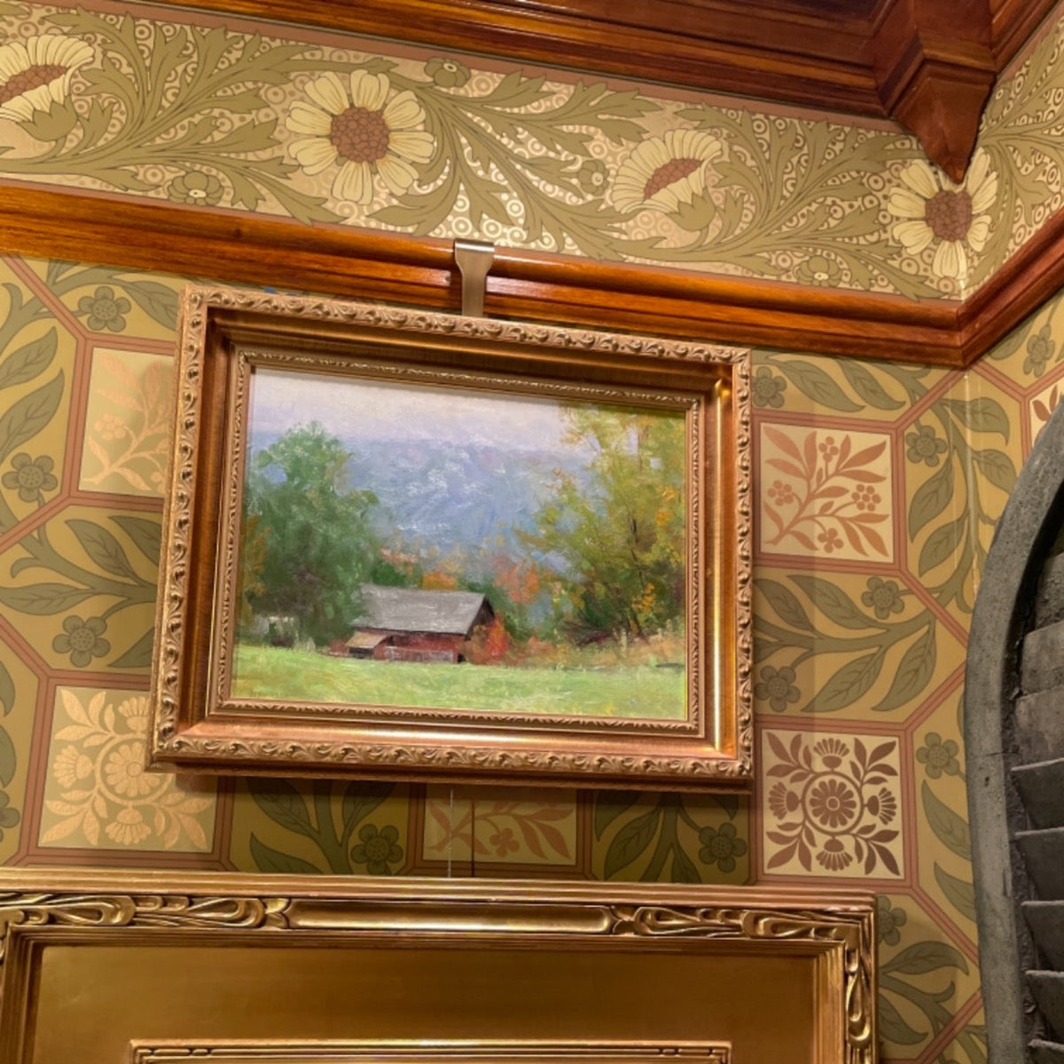 Two framed paintings of landscapes on a decorative wall with floral wallpaper.